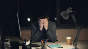 Stressed man holding his head at a desk late at night, illustrating the psychology of procrastination and burnout