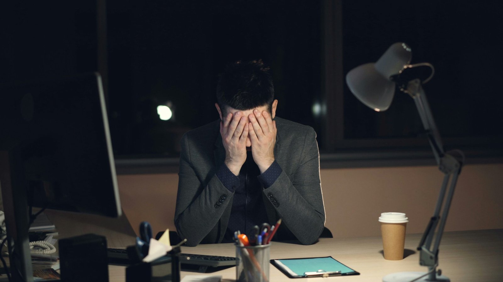 Stressed man holding his head at a desk late at night, illustrating the psychology of procrastination and burnout