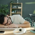 Man sleeping at his desk with headphones and coffee, illustrating the perfect 20-minute power nap technique