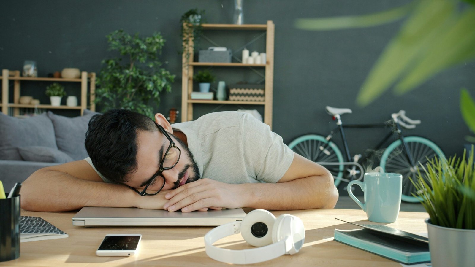 Man sleeping at his desk with headphones and coffee, illustrating the perfect 20-minute power nap technique